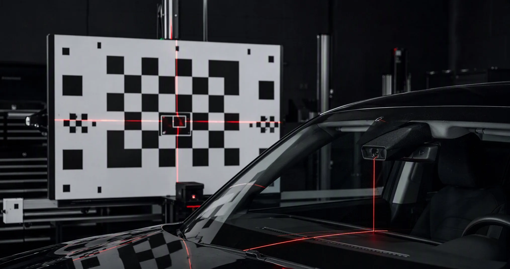 A vehicle facing an ADAS calibration target board, with red alignment lasers across the windshield camera